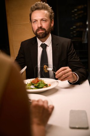 Photo for Elegant man with a beard is having dinner in a restaurant, opposite is a female - Royalty Free Image