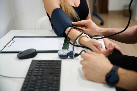 Foto de Médico mide una presión arterial de los pacientes en una recepción, el examen se lleva a cabo en un consultorio brillante - Imagen libre de derechos