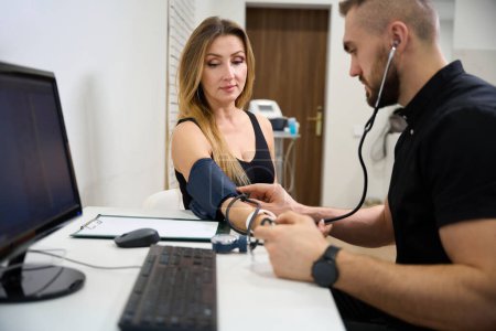 Foto de Fisioterapeuta mide una presión arterial de los pacientes en una cita, el examen se lleva a cabo en un consultorio brillante - Imagen libre de derechos