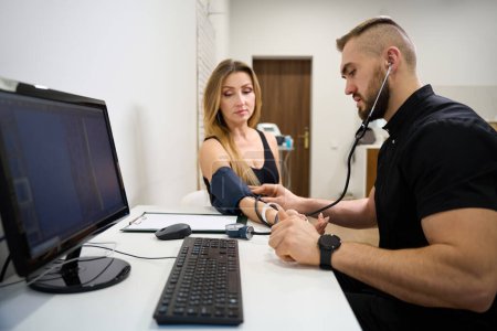 Foto de Fisioterapeuta médico mide la presión arterial de un paciente en una recepción, el examen se lleva a cabo en un consultorio brillante - Imagen libre de derechos