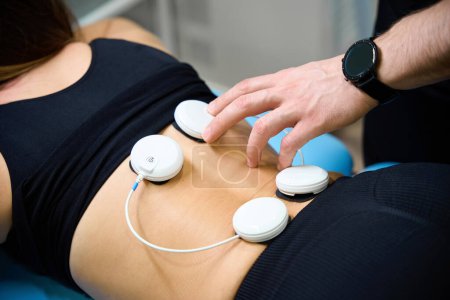 Photo for Doctor uses muscle electrical stimulator for wellness procedure in a rehabilitation center, a patient is being treated for her back - Royalty Free Image