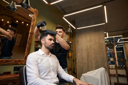 Téléchargez les photos : Coiffeur habile créant un nouveau look avec des ciseaux dans le salon de coiffure professionnel - en image libre de droit