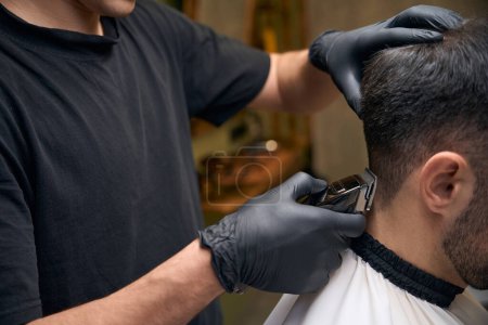 Téléchargez les photos : Coiffeur homme faisant coupe de cheveux pour le client au salon de coiffure - en image libre de droit