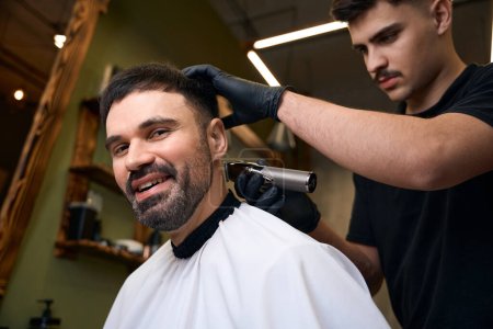 Téléchargez les photos : Maître coiffeur faire des soins et un nouveau look de coiffure pour le client masculin au salon de coiffure - en image libre de droit