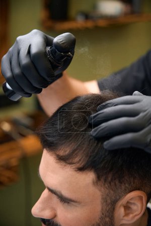Téléchargez les photos : Gros plan de coiffeur utilisant pulvérisation pour faire coiffure pour le client au salon de coiffure - en image libre de droit