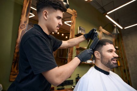Téléchargez les photos : Coiffeur faisant coiffure cheveux pour homme client au salon de coiffure - en image libre de droit