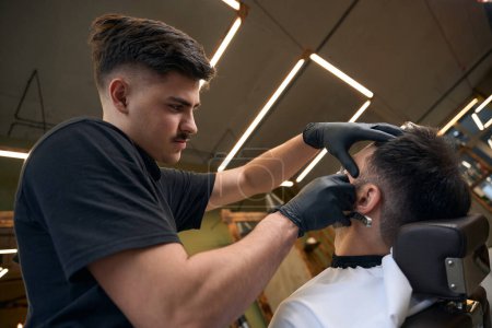 Téléchargez les photos : Barbier maître faire coiffage de la barbe pour le client dans le salon de coiffure - en image libre de droit