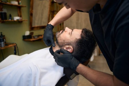 Photo for Barber trimming mans beard in professional barbershop - Royalty Free Image