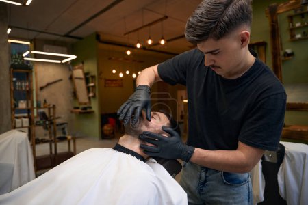 Téléchargez les photos : Homme barbu se rasé avec rasoir à bord droit par coiffeur au salon de coiffure - en image libre de droit