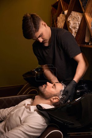 Photo for Hairdresser man washing client head with shampoo in barbershop - Royalty Free Image