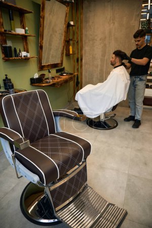 Téléchargez les photos : Coiffeur couper les cheveux du client masculin sur son lieu de travail dans le salon de coiffure - en image libre de droit