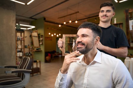Téléchargez les photos : Coiffeur en colère le résultat de son travail au client dans le salon de coiffure - en image libre de droit