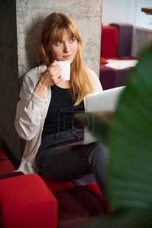 Téléchargez les photos : Créateur de vêtements femme d'affaires utilisant un ordinateur portable pour créer une collection élégante et boire du café - en image libre de droit