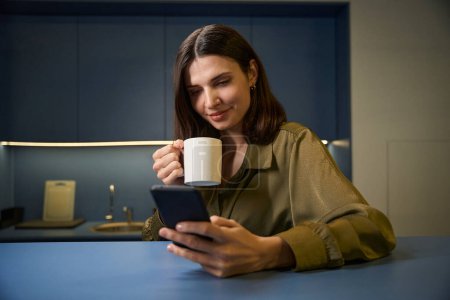 Téléchargez les photos : Femme gaie écrivant à l'aide d'un smartphone tout en faisant une pause café au bureau - en image libre de droit