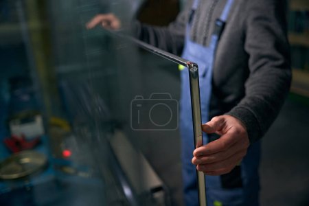 Photo for Worker at a window production carries out the initial sealing of the spacer frame, a man in a work suit - Royalty Free Image