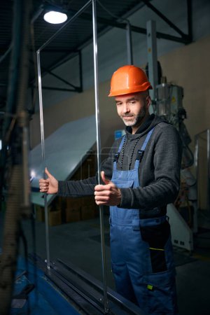 Foto de Master trabaja con un marco espaciador en la producción de una ventana, un hombre con un casco protector - Imagen libre de derechos