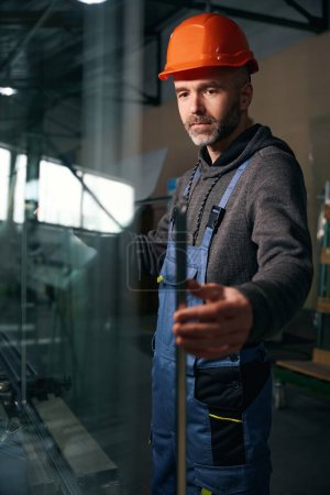 Foto de Trabajador de mediana edad en un taller de producción con un casco de seguridad naranja, el hombre tiene una barba - Imagen libre de derechos