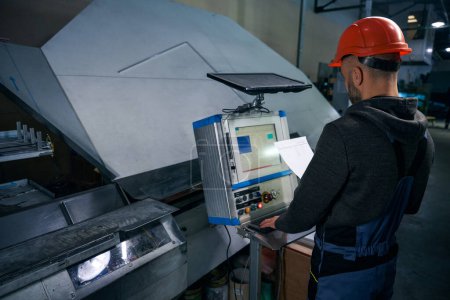 Hombre trabaja con documentación de producción en el lugar de trabajo, equipo de alta tecnología se utiliza en la producción