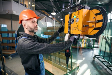 Arbeiter benutzt ein Vakuumhebegerät in einer Fensterproduktion, ein Mann in Overalls
