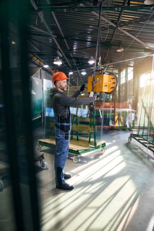 Foto de Macho utiliza un dispositivo de elevación al vacío para trabajar con doble acristalamiento, un hombre con mono - Imagen libre de derechos