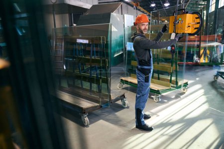Foto de Hombre usando un dispositivo de elevación al vacío en un taller de producción, un hombre usando overoles - Imagen libre de derechos