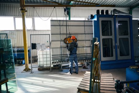 Foto de Trabajador en una producción de ventanas utiliza equipos modernos, un hombre con un casco de seguridad naranja - Imagen libre de derechos