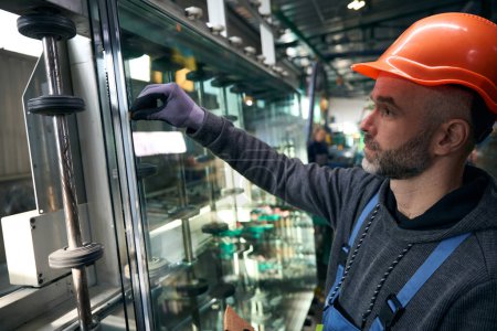 Téléchargez les photos : Travailleur utilise des outils spéciaux pour travailler avec le verre dans la production de fenêtres, un homme portant un casque de sécurité - en image libre de droit