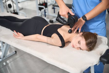 Photo for Kinesiologist massages the body of a patient, he uses a special massager - Royalty Free Image