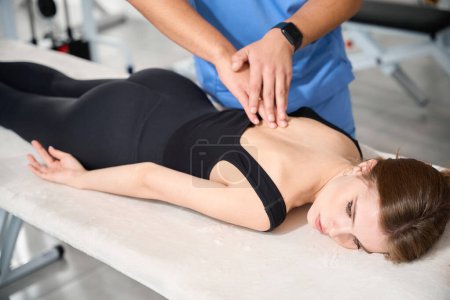 Physiotherapeutin arbeitet mit junger Wirbelsäule, Frau liegt auf Magen auf Massagetisch
