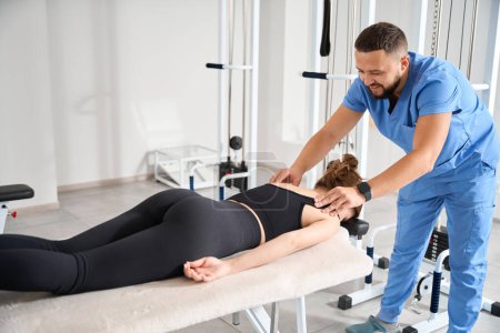 Téléchargez les photos : Homme sur le lieu de travail redresse le dos d'une jeune femme, une femme s'allonge sur le ventre sur une table de massage - en image libre de droit