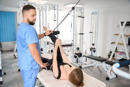 Téléchargez les photos : Médecin physiothérapeute utilise une machine d'exercice spéciale pour travailler avec un patient, la femme s'allonge sur une table de massage - en image libre de droit