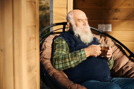 Foto de Viejo barbudo se encuentra en la terraza con una taza de té, él está sentado en una silla cómoda - Imagen libre de derechos