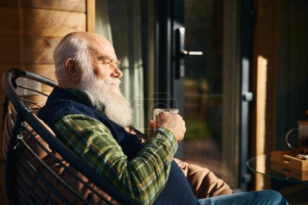 Foto de Hombre mayor está sentado en la terraza con una taza de té, él está sentado en una silla cómoda - Imagen libre de derechos