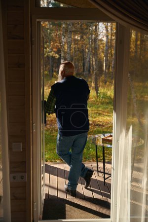 Elderly man admires nature with a cup of tea, he is in comfortable casual clothes