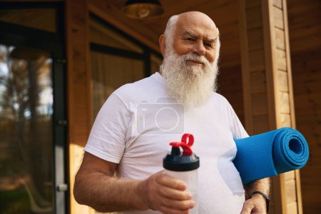 Téléchargez les photos : Homme âgé a quitté la maison pour des exercices matinaux avec un karimat et une bouteille d'eau - en image libre de droit