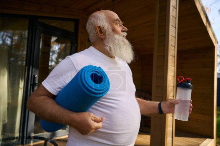 Téléchargez les photos : Le vieil homme a quitté la maison pour des exercices matinaux avec une bouteille d'eau et un karimat - en image libre de droit
