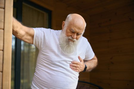 Téléchargez les photos : Le vieil homme souffre de douleurs cardiaques, il se tient sur la véranda d'une maison de campagne - en image libre de droit
