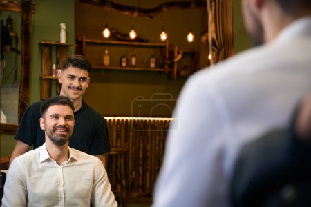 Téléchargez les photos : Barbier qualifié avec ciseaux brandissant artisanat coiffure élégante pour son client dans le salon de coiffure - en image libre de droit