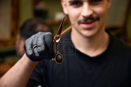 Photo for Barber with mustache showing his scissors professional equipment in barbershop - Royalty Free Image
