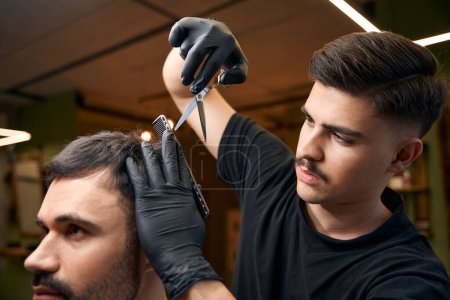 Téléchargez les photos : Barbier utilisant des ciseaux pour coiffer les cheveux de son client dans le salon de coiffure professionnel - en image libre de droit
