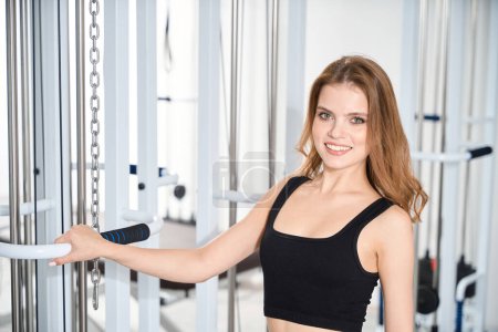 Téléchargez les photos : Charmante jeune femme se tient près de la machine d'exercice, femelle dans une combinaison d'entraînement confortable - en image libre de droit