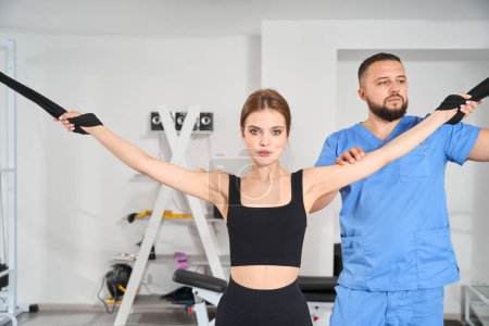 Téléchargez les photos : Femme fait des exercices d'étirement musculaire sous la supervision d'un physiothérapeute à l'aide d'un dispositif spécial - en image libre de droit