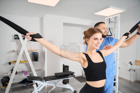 Female doing muscle stretching exercises under the supervision of a physiotherapist using a special device