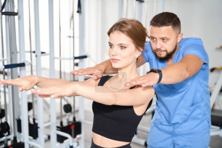 Téléchargez les photos : Spécialiste surveille les exercices d'une jeune femme, les cours ont lieu dans la salle de gym - en image libre de droit