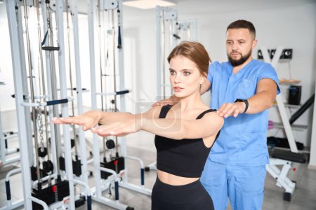 Physiotherapeut überwacht die Übungen einer jungen Frau, Unterricht findet in der Turnhalle statt