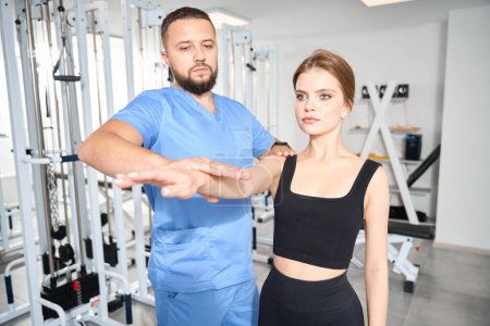 Téléchargez les photos : Jeune chiropraticien forme posture correcte à une patiente, les cours sont tenus dans la salle de gym - en image libre de droit