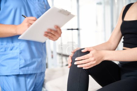 Téléchargez les photos : Le médecin interroge une femme dans une clinique de kinésiologie, la femme se plaint de douleurs au genou - en image libre de droit