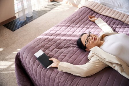 Téléchargez les photos : Femme d'affaires satisfaite avec des documents de voyage à la main couchée sur le lit dans sa suite - en image libre de droit