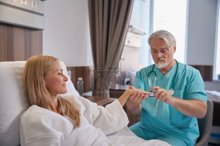 Stationär im Krankenhausbett liegend, während der behandelnde Arzt ihr ein Pulsoximeter auf die Fingerkuppe legt