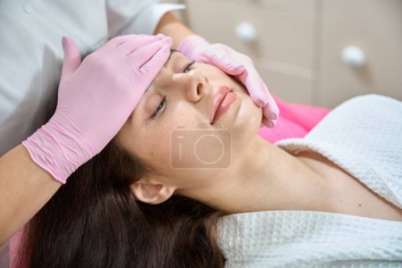 Photo for Cropped photo of female lying supine while doctor in nitrile gloves massaging her face - Royalty Free Image